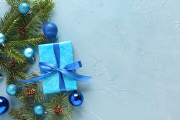 Composition with fir tree branches, gift box and Christmas balls on blue background