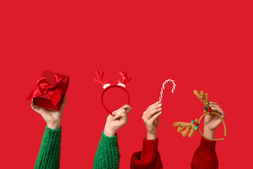 Female hands with Christmas reindeer horns headbands, gift box and candy cane on red background