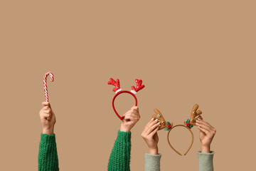 Female hands holding Christmas reindeer horns headbands and candy cane on beige background