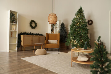 Interior of living room with table, armchair and Christmas trees near light wall
