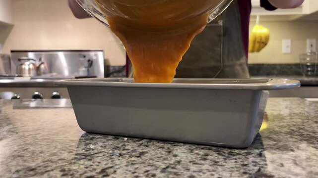 Close Up of Man Pouring Pumpkin Bread Batter into Loaf Pan in Home Kitchen