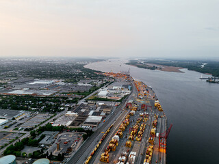 Fototapeta premium Aerial view of Montreal port with cargo containers, cranes and city skyline at sunset. g.