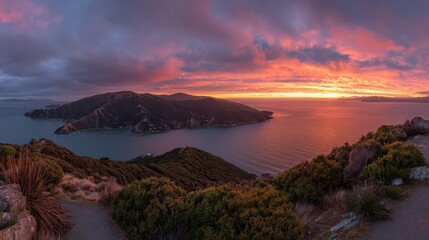 Obraz premium A stunning panoramic view of a coastal landscape at sunset, featuring vibrant colors reflecting on the water and rugged hills in the foreground.