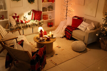 Interior of dark living room decorated for Christmas with sofa, armchairs and glowing lamps