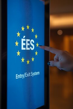 Modern EU Entry Exit System touchscreen kiosk being operated by a traveler, showing digital border control technology and biometric registration interface