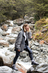 A woman hiking across rocky stones beside a mountain river in Arthurs Pass, New Zealand.