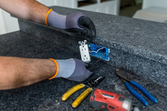 Electrician replacing GFCI outlet on black kitchen island countertop, Florida, USA