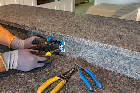 Electrician installing black GFCI outlet on granite kitchen island, Florida, USA