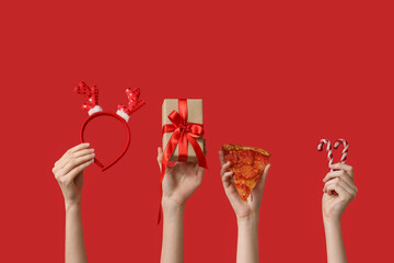Female hands with pizza slice, reindeer horns headband, candies and gift boxes on red background