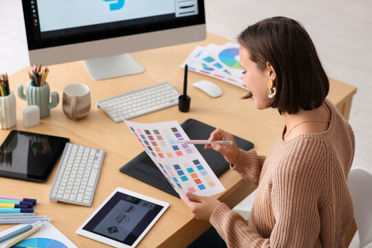 Young female graphic designer working with color samples at table in office - Powered by Adobe