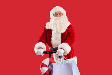 Santa Claus with modern electric kick scooter and shopping bags on red background. Christmas celebration