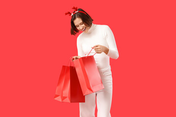 Beautiful young happy woman in reindeer horns with shopping bags on red background. Christmas celebration