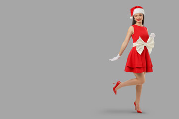 Woman wearing a red dress and Santa hat stands elegantly, smiling
