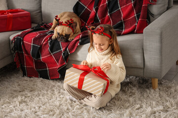 Cute little girl with French bulldog and Christmas gift sitting on floor at home