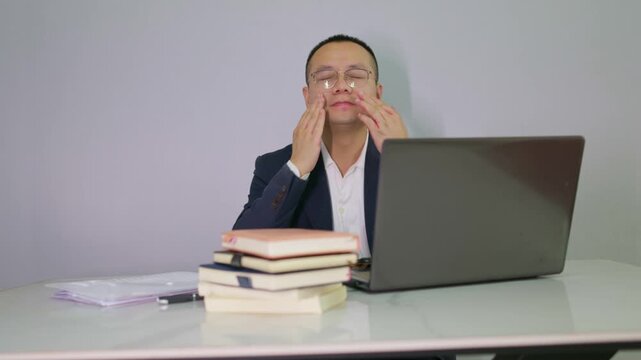 Mature man who works long hours in front of a computer feels discomfort in his eyes. The overworked office worker massages his uncomfortable eyes.