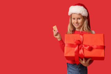 Cute girl in Santa hat with gift box and credit card on red background. Christmas celebration