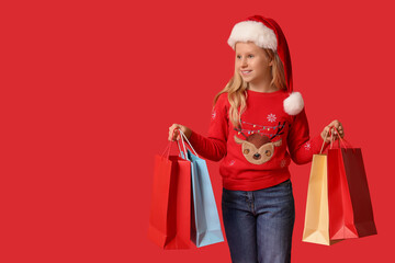 Cute girl in Santa hat with shopping bags on red background. Christmas celebration