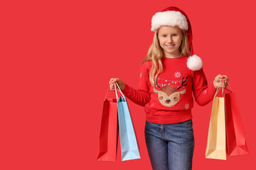 Cute girl in Santa hat with shopping bags on red background. Christmas celebration
