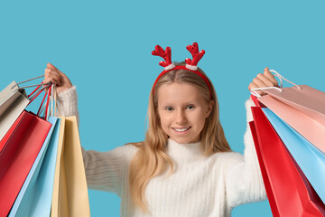 Cute girl in reindeer horns with shopping bags on blue background. Christmas celebration