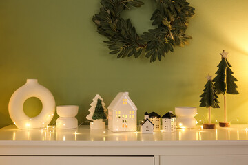 House shaped candle holders with glowing Christmas lights on shelf near green wall