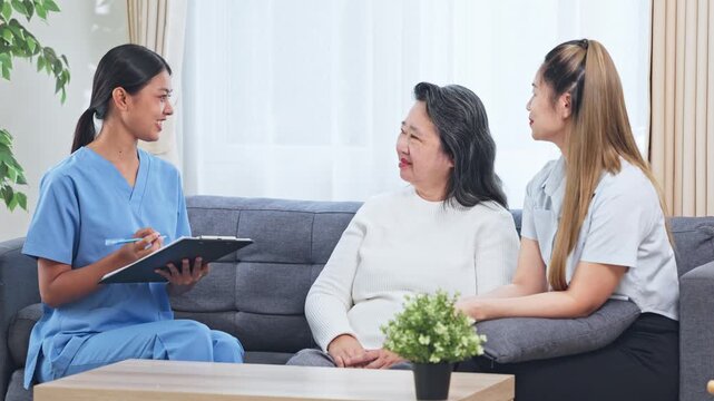 Asian Elderly woman caregiver consultation living room with nurse clipboard and supportive care compassionate home visit interview showing attentive healthcare assessment and family support during