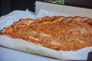 Freshly baked flatbread with golden crust and sesame seeds, displayed on white baking paper at a local bakery in Granada, Spain. traditional pastry