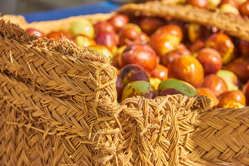 Close-up of a rustic woven basket filled with ripe jujube fruits in warm sunlight at a market in Granada, Spain. harvest scene