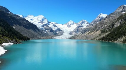 Slow rising aerial shot revealing a pristine turquoise glacier lake surrounded by towering snow-capped mountain peaks on a clear day untouched, environment, glacier lake - Powered by Adobe