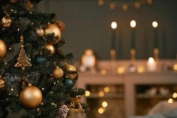 Christmas tree decorated with gold ornaments and lights standing in foreground, blurred background showing glowing candles and festive decorations creating holiday ambiance