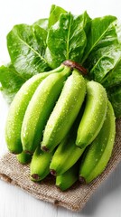 Obraz premium Fresh Green Bananas with Leaves and Water Droplets on Burlap Fabric