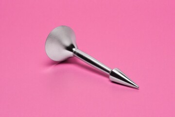 Shiny metal applicator lying on a bright pink surface in a studio setting, illuminated by soft studio light