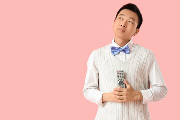 Thoughtful young Asian man with TV remote controller on pink background