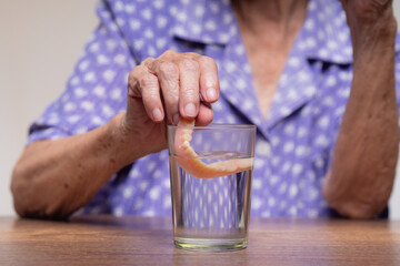 Elderly woman cleaning dental dentures in glass of water.