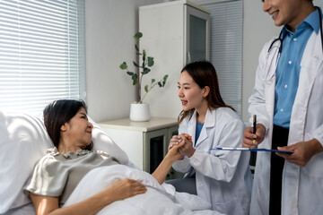 Asian female doctor holding patient's hand, offering support and empathy during hospital bedside...