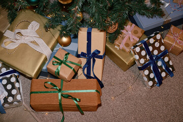 Christmas tree branches hanging above multiple wrapped gift boxes with ribbons arranged on carpeted...