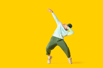 Young man dancing hip-hop on yellow background