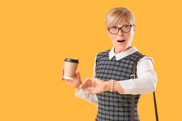 Shocked mature businesswoman with wristwatch and coffee on yellow background. Time management