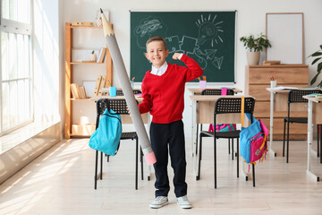 Cute little schoolboy with large pencil showing muscles in classroom