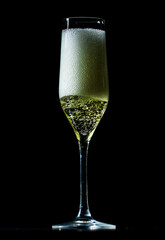 Champagne sparkling in a crystal glass. Pouring bubbly champagne with festive bubbles. Close-up of sparkling wine splash in elegant wineglass. Champagne drink with golden fizz on black background.