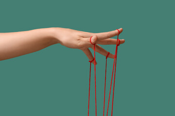 Female hand of puppeteer with red strings on green background © Pixel-Shot