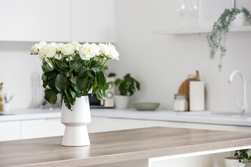 Vase with white roses on table in kitchen