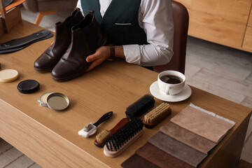 Male shoemaker with polished leather boots at table in workshop