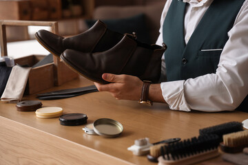 Male shoemaker with polished leather boots at table in workshop, closeup