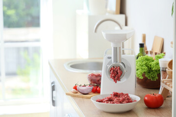 Modern meat grinder with minced beef and vegetables on counter in kitchen