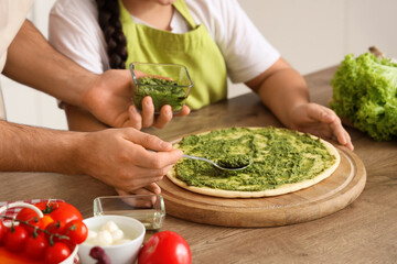 Little girl with her father applying pesto sauce on pizza dough in kitchen, closeup