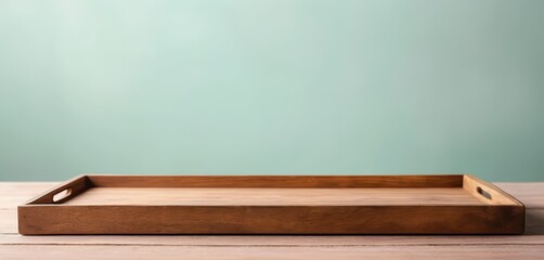 A wooden serving tray with handles rests on a light colored wooden surface against a soft teal background