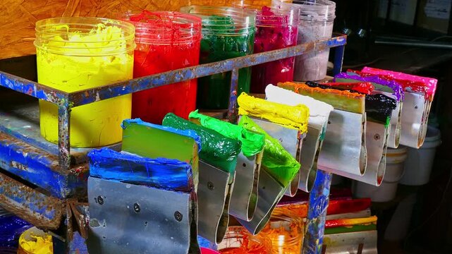 Colorful Ink for Screen Printing Factories
Inside a busy Tee shirt factory plastisol inks in multiple tones bright and dark are neatly arranged for industrial use. Workers use handmade tools handles