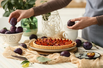 Woman with tasty plum pie and fresh fruits at table in kitchen