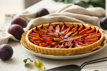 Plate with tasty plum pie with spatula on table in kitchen