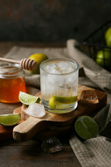 Glass of lime infused water and jar of honey on wooden table
